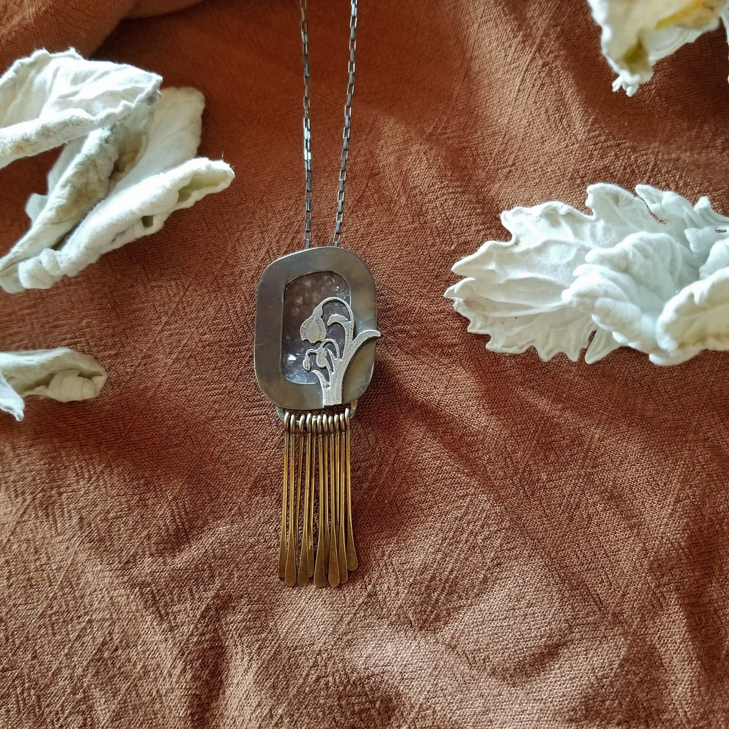 Snowdrop Necklace No. 3 - A retangular amethyst druzy (pale purple) set in a sterling silver box frame. A hand pierced and hand engraved snowdrop is soldered on the bottm left. Handmade brass fringe hangs below the box frame. All hanging on a sterling silver chain.