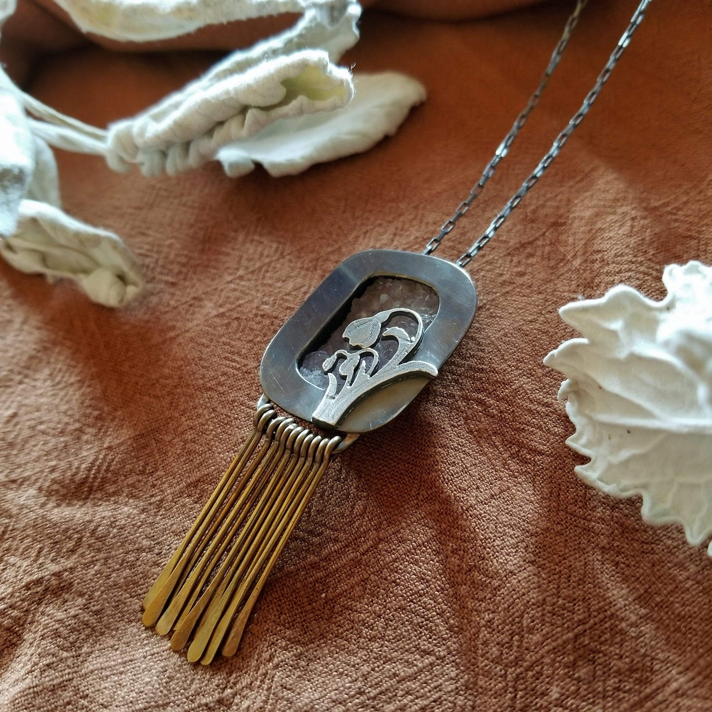 Right side angle Clost up - Snowdrop Necklace No. 3 - A rectangular amethyst druzy (pale purple) set in a sterling silver box frame. A hand pierced and hand engraved snowdrop is soldered on the bottm left. Handmade brass fringe hangs below the box frame. All hanging on a sterling silver chain.
