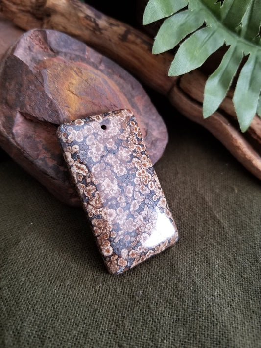 Fossilized coral rectangular bead with black, grey, and brown tones.