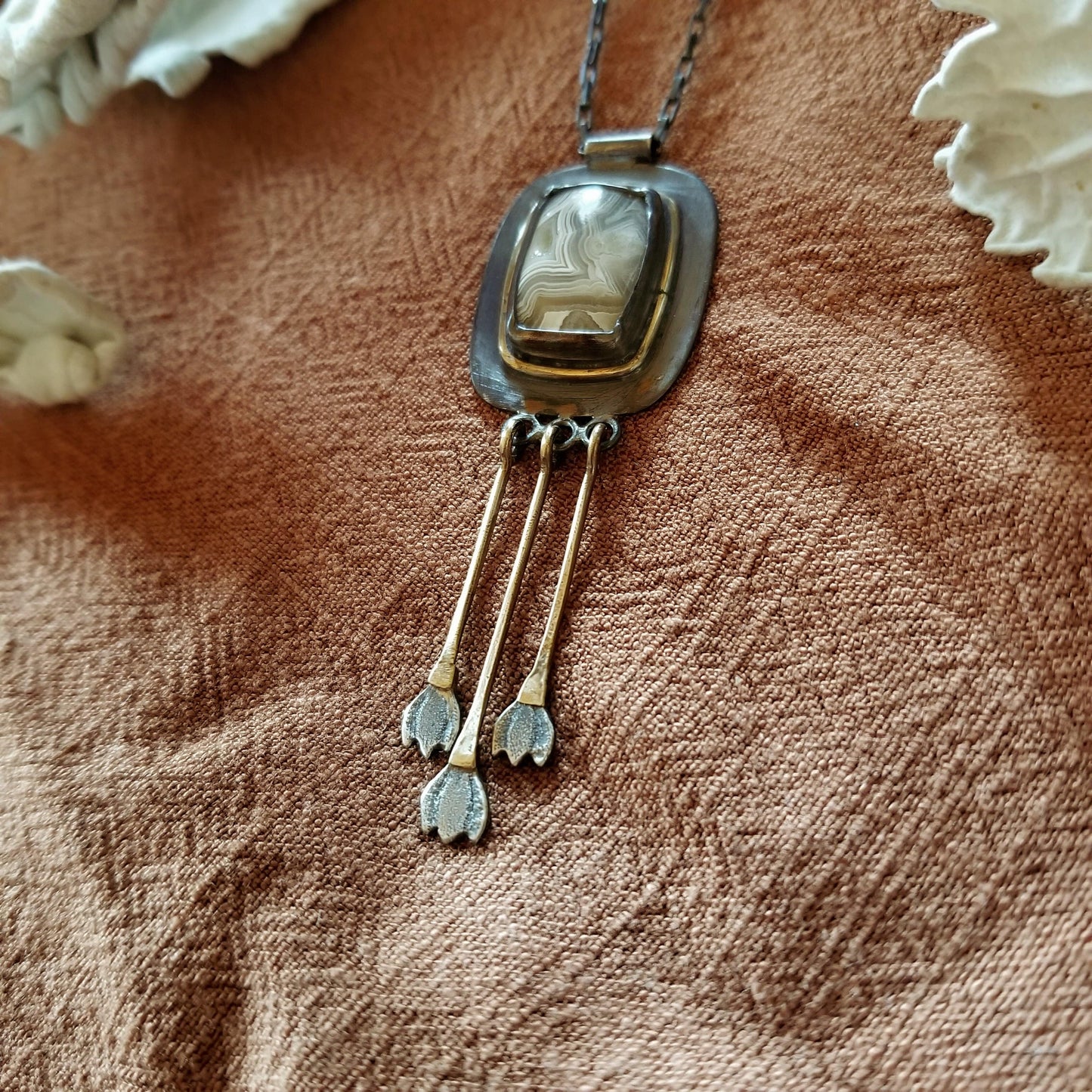 View from above right side - Snowdrop Necklace No. 1 - Cushion cut (rounded rectangle) Mexican Agate set in sterling silver and brass with 3 individual hand engraved snowdrop flowers hanging from brass fringe. All hanging from a sterling silver box chain. 