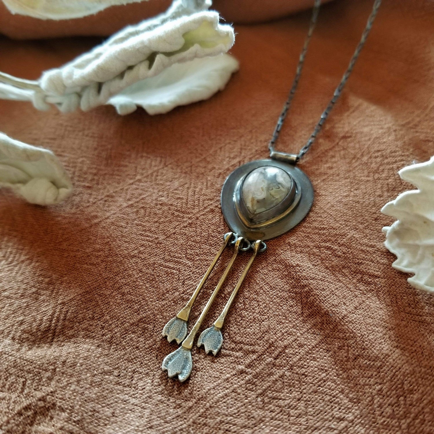 Handmade one of a kind sterling silver and brass necklace. Tear drop Mexican Agate (white and grey colors) set in sterling silver and brass with 3 individual hand engraved snowdrop flowers hanging from brass fringe. All hanging from a sterling silver box chain. 
