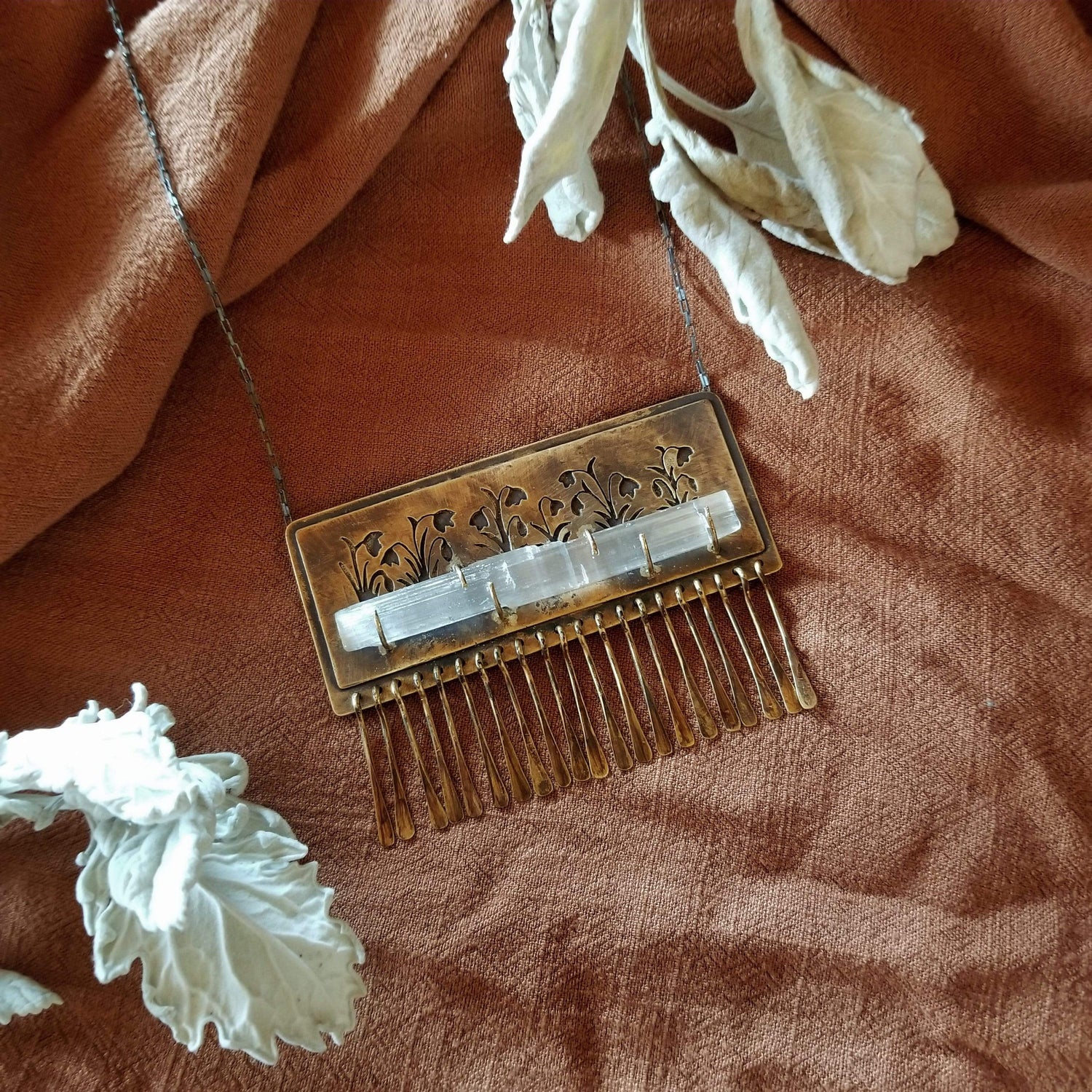 Handmade one of a kind necklace made with brass, sterling silver, and selenite. Brass is hand pierced with a meadow of snowdrop flowers sitting on top of a pronged set selenite wand. Hammered brass paddle fringe hang below. All hanging on a sterling silver chain.