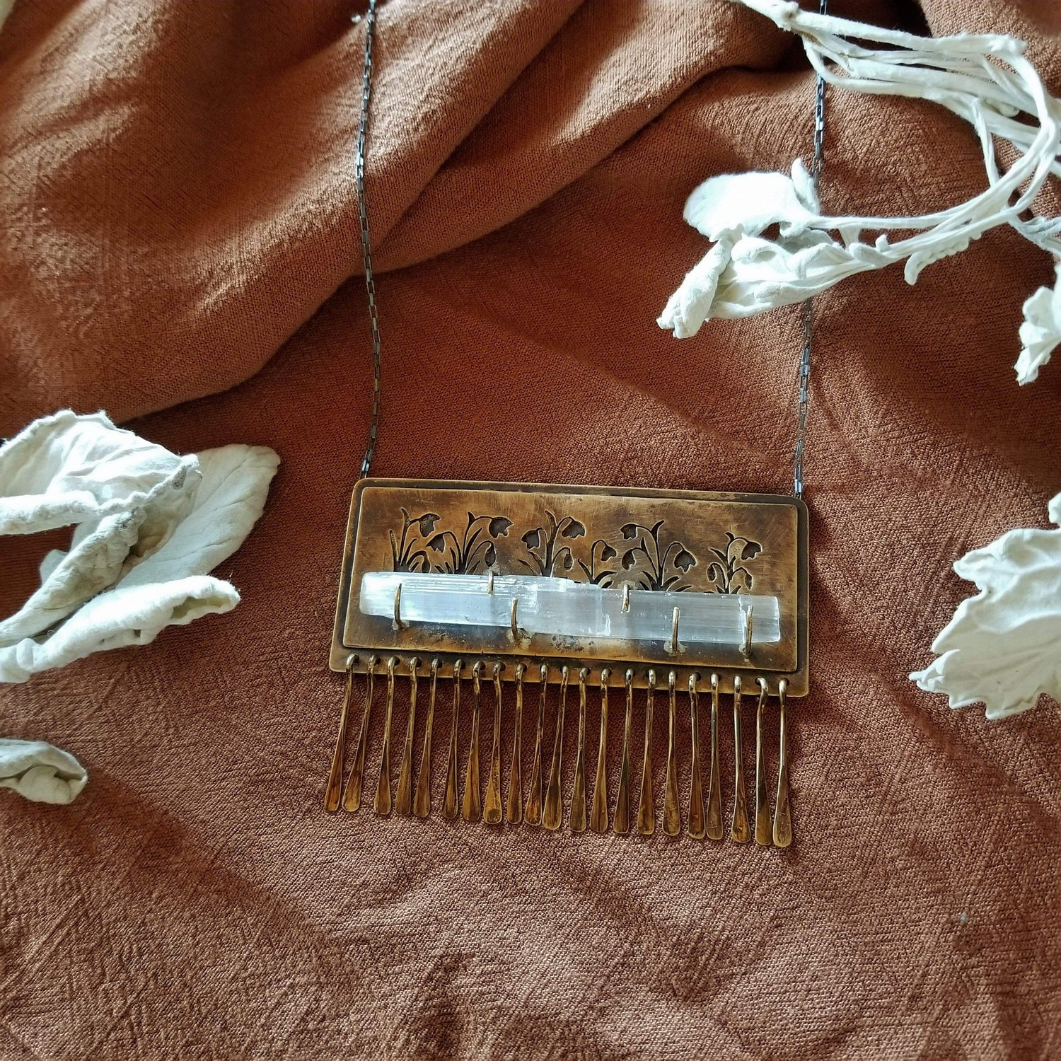 Handmade one of a kind necklace made with brass, sterling silver, and selenite. Brass is hand pierced with a meadow of snowdrop flowers sitting on top of a pronged set selenite wand. Hammered brass paddle fringe hang below. All hanging on a sterling silver chain.