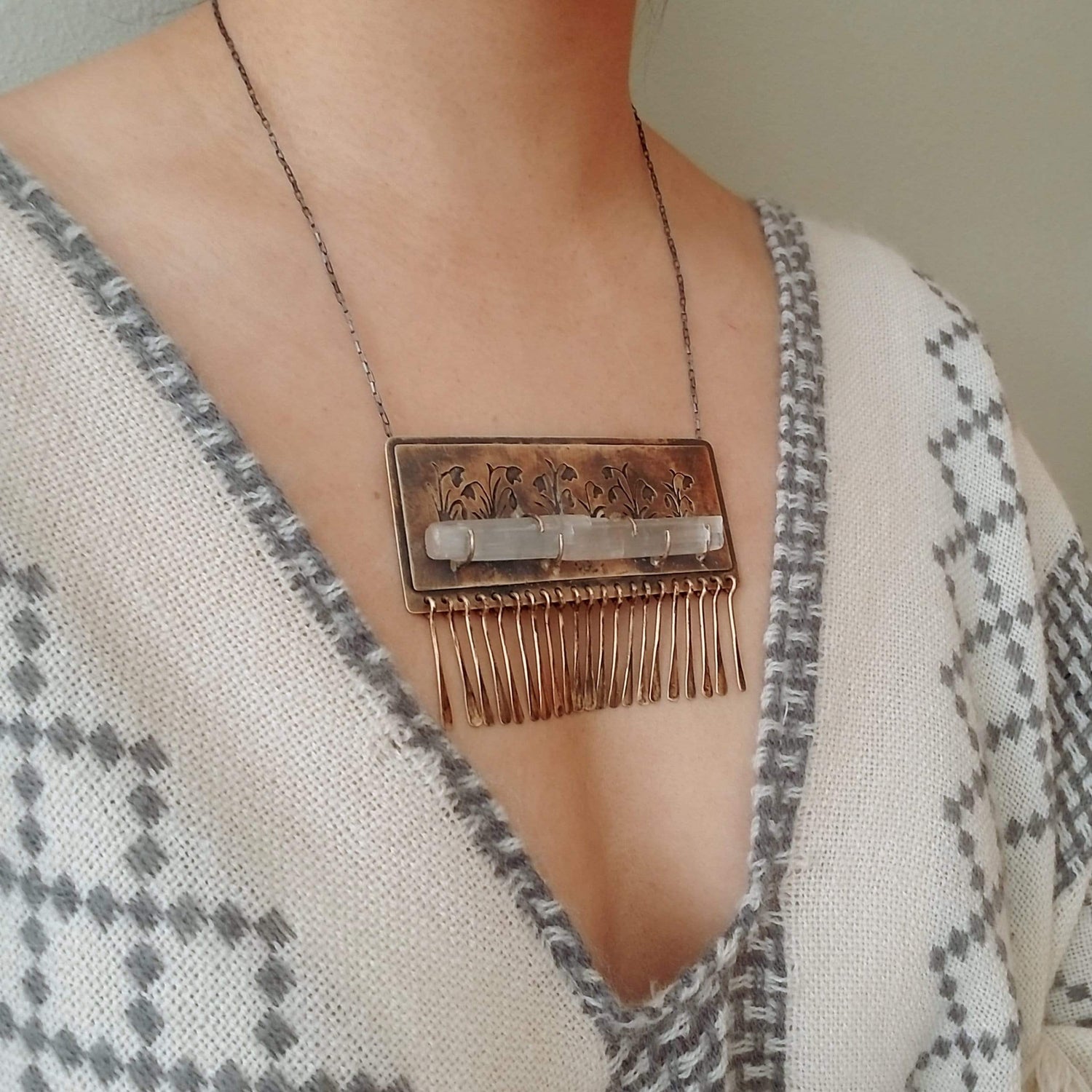 Handmade one of a kind necklace made with brass, sterling silver, and selenite. Brass is hand pierced with a meadow of snowdrop flowers sitting on top of a pronged set selenite wand. Hammered brass paddle fringe hang below. All hanging on a sterling silver chain.